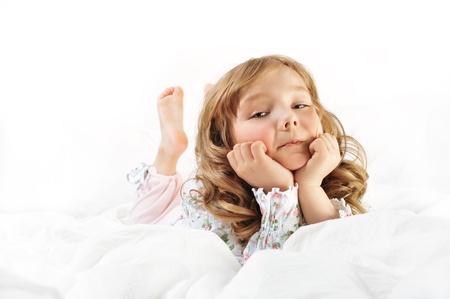 Closeup portrait of adorable little girl with beautiful long curly hair resting in her bed with white linenの写真素材