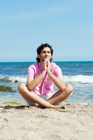 Portrait of young man sitting in lotus pose on sand on beach and meditating. Mediterranean sea at backgroundの写真素材
