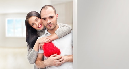 Portrait of young couple with red heart standing at their home and embracing. They are really happy to be together. Lots of copyspace for your needsの写真素材