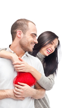 Happy young adult couple with red heart on white background, embracing and laughingの写真素材