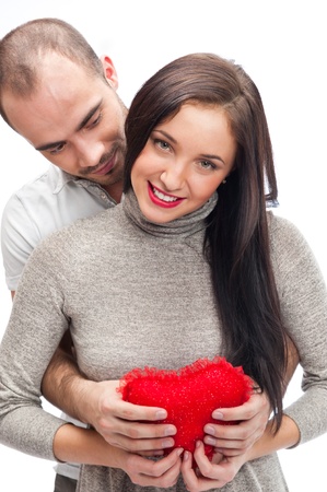 Happy young adult couple with red heart on white background, embracing and laughingの写真素材