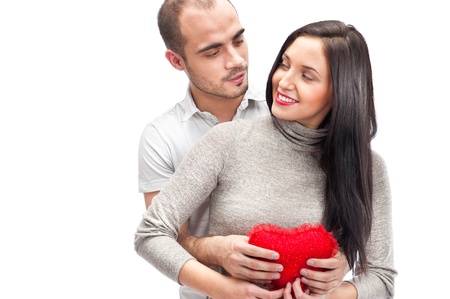 Happy young adult couple with red heart on white background, embracing and laughingの写真素材