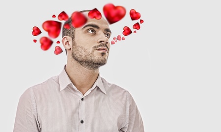Young man thinking about love. Red hearts are flying around his headの写真素材