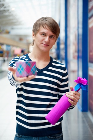 Portrait of young man inside shopping mall standing relaxed and holding gift box and bottle. He is preparing to visit his girlfriend and make a proposalの写真素材