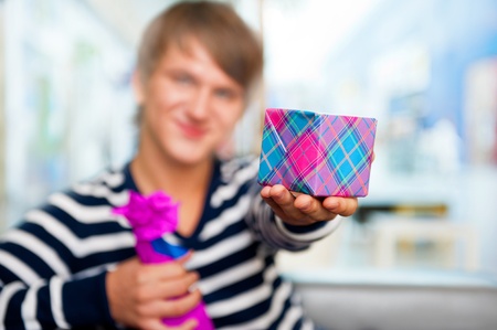 Portrait of young man inside shopping mall standing relaxed and holding gift box and bottle. He is preparing to visit his girlfriend and make a proposalの写真素材