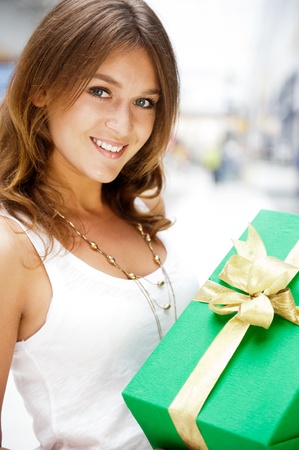Portrait of young excited pretty woman standing inside shopping mall smiling and holding christmas gift.の写真素材