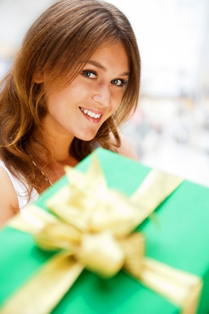 Portrait of young excited pretty woman standing inside shopping mall smiling and holding christmas gift on foreground.の写真素材