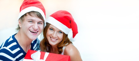 Young happy couple in Christmas hats standing together and holding christmas gifts