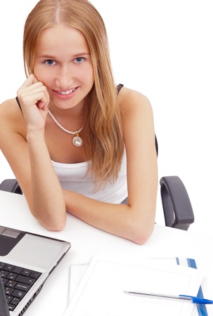 Portrait of a pretty female student with laptop and exercise book sitting at her desk looking at camera against white backgroundの写真素材