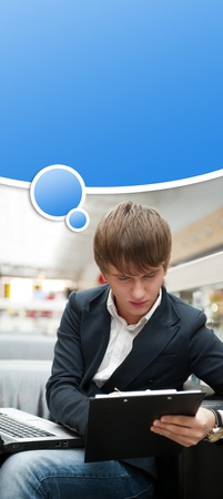 Portrait of handsome young man working with laptop at cafe at business center hall. Blank graphic balloon with his thoughts overheadの写真素材