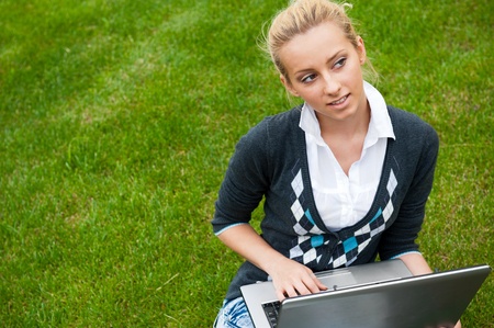 Beautiful young woman using laptop at outdoor. Looking away, daydreaming. Horizontal shotの写真素材