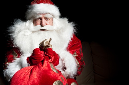 Santa sitting at the Christmas room and looking into the sackの写真素材