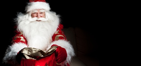 Santa sitting at the Christmas room and looking into the sackの写真素材