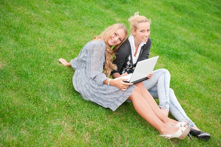 Portrait of two smiling women using laptop on a green meadow at the city park. Copyspaceの写真素材