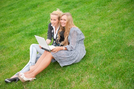 Portrait of two smiling women using laptop on a green meadow at the city park. Copyspaceの写真素材