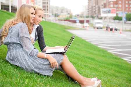 Portrait of two smiling women using laptop on a green meadow at the city parkの写真素材