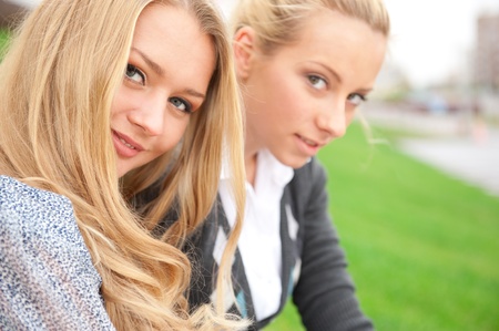Two women hugging and smiling sitting on the grass at city parkの写真素材
