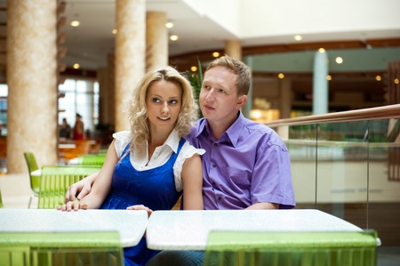 Portrait of a happy young couple looking away while sitting near a table at mall and planning purchasesの写真素材
