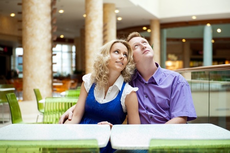 Portrait of a happy young couple looking away while sitting near a table at mall and planning purchasesの写真素材
