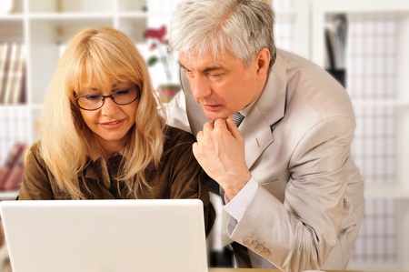A confident smiling business woman with her colleague at modern comfortable office working using laptopの写真素材