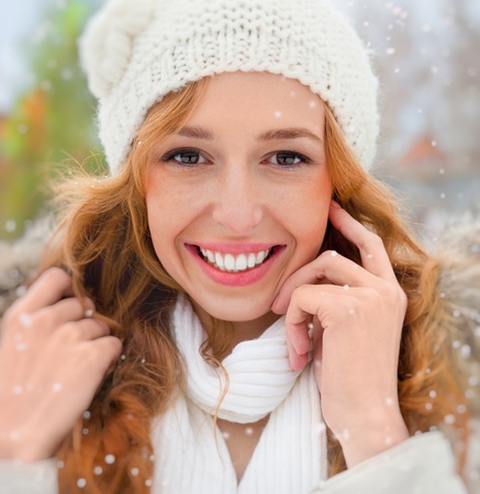 Portrait of beautiful young red hair woman outdoors in winter looking at camera and enjoying snowの写真素材