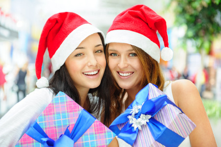 Young happy girls in Christmas hats.Standing together indoors and holding gift boxesの写真素材