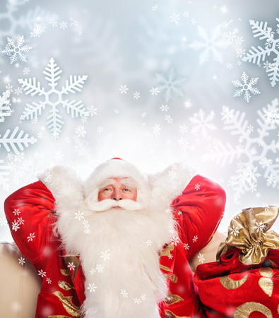 Santa Claus sitting with a sack indoor relaxing on silwer snowflakes backgroundの写真素材