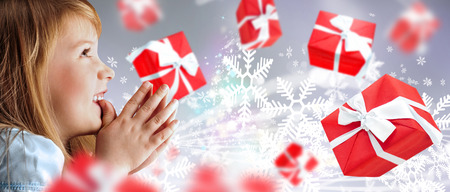 Portrait of young smiling praying girl looking up against silver fairy snowstorm background  Red gift boxes are flying aroundの写真素材