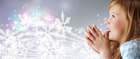 Portrait of young smiling praying girl looking up in blue dress against silver fairy snowstorm backgroundの写真素材