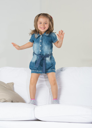 Adorable little girl jumping at home on sofaの写真素材