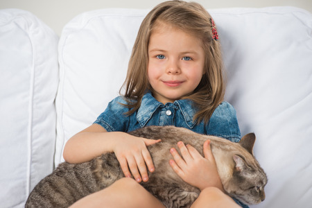 Cute little girl hugging tabby cat with love, looking at camera.の写真素材