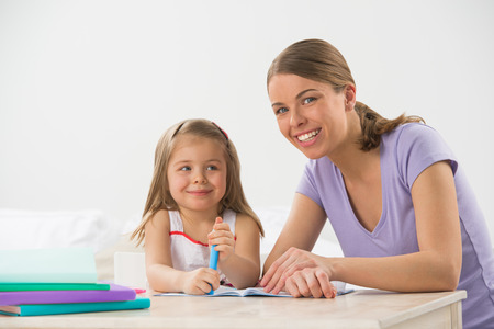 Mother and daughter at home. Mom teachs little girl to draw and writeの写真素材