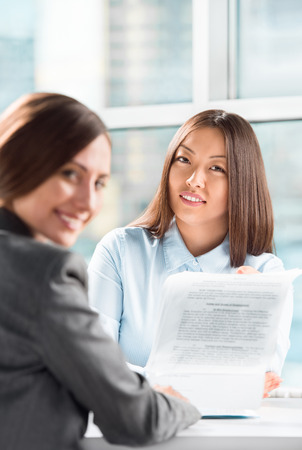 Two business women talking and signing contract at officeの写真素材