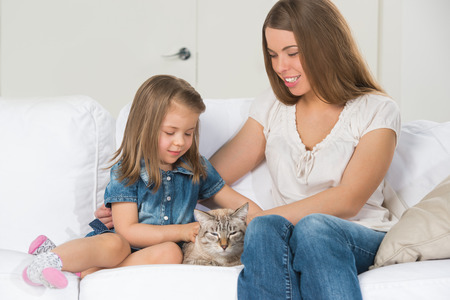 Mother and daughter sitting on sofa and cuddling catの写真素材