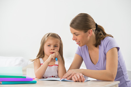 Mother and daughter at home. Mom teachs little girl to draw and writeの写真素材