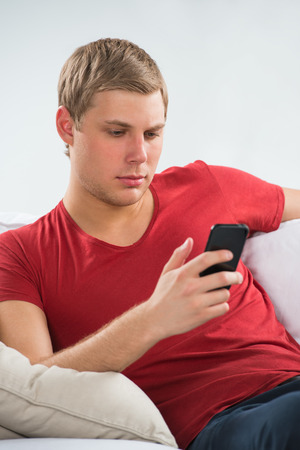 Young man using mobile phone to send short message and watch news in social mediaの写真素材