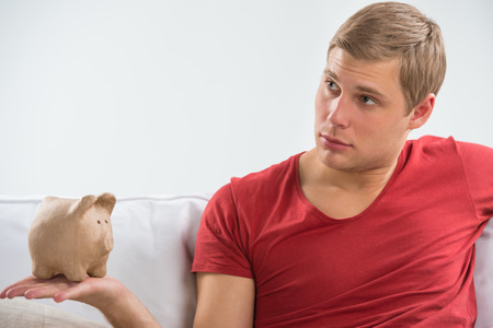 Man holding up piggy bank at home and looking to copyspaceの写真素材