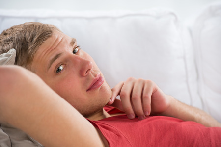 Portrait of a happy young man laying on sofa in thoughtの写真素材