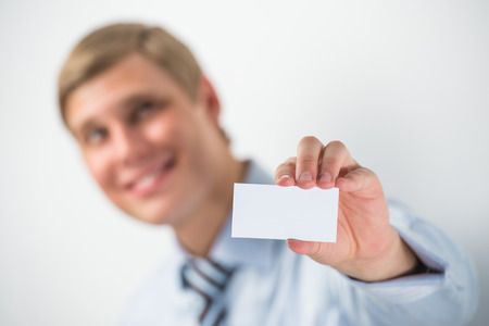 Happy smiling business man showing blank businesscard and dreaming, while leaning on wall at officeの写真素材
