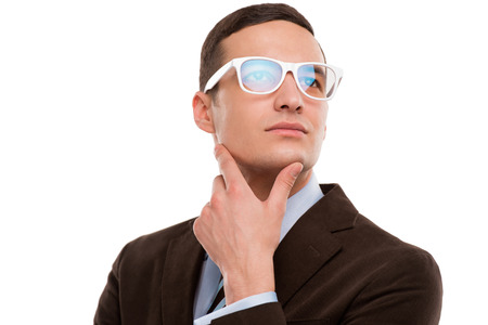 Young thoughtful businessman wearing glasses and holding chin on hand on white backgroundの写真素材