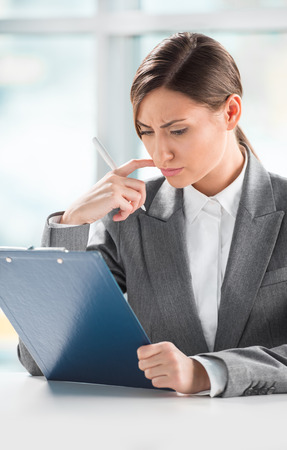 Front view of business woman looking over papers on clipboard at her officeの写真素材