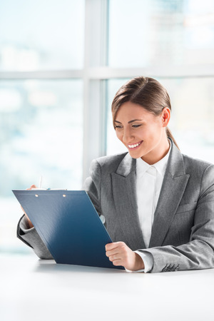 Front view of business woman looking over papers on clipboard at her officeの写真素材