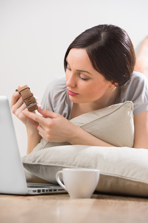 A young woman lying on the floor in front of her laptop and chatting with her boyfriend, showing to him a gift using online messenger and built-in cameraの写真素材