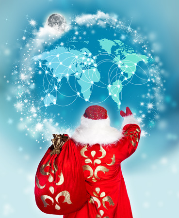 Santa Claus preparing for Christmas. He is looking at digital worldmap to see children list to greet with gifts. Modern technologies in traditional events conceptの写真素材