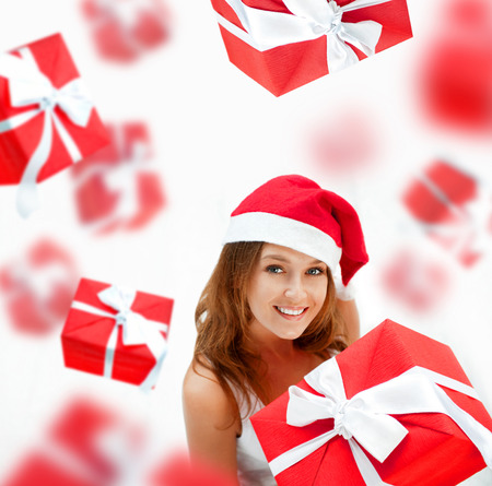 Young woman holding gift box wearing santa claus hat. Many gift boxes falling down around herの写真素材