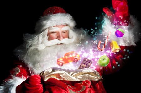 Santa Claus getting gifts and confection from his bag and showing miracleの写真素材