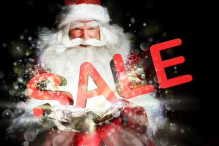 Santa Claus holding his bag and smiling. Lights and sparks are flying from the bag. Sale sign in front of Santaの写真素材