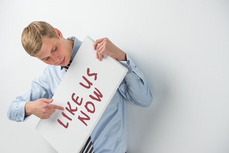 Handsome businessman showing "like us now" text on a billboardの写真素材