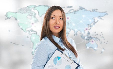 Asian business woman holding reports and smiling against world map background. Copyspaceの写真素材