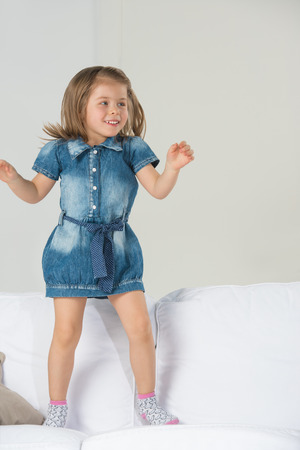 Adorable little girl jumping at home on sofaの写真素材